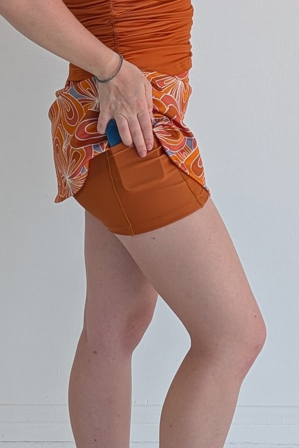 Form Fitting burnt orange miniskirt with 70's inspired flower print and built in shorts and pockets; great for gameday or hanging out with friends.