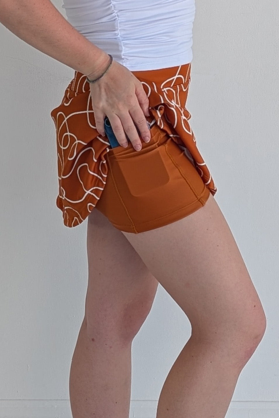 Relaxed back burnt orange miniskirt with scribbles print and built in shorts and pockets; great for gameday or hanging out with friends.