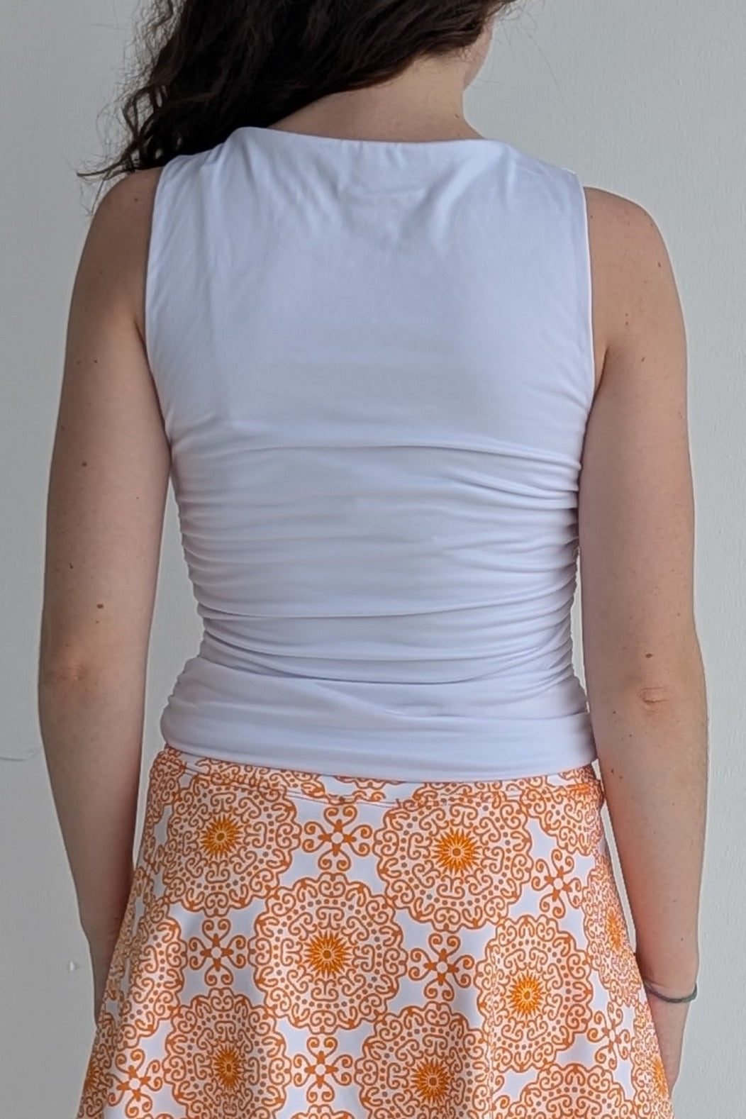 Person wearing a white sleeveless top and an orange patterned skirt on a plain background