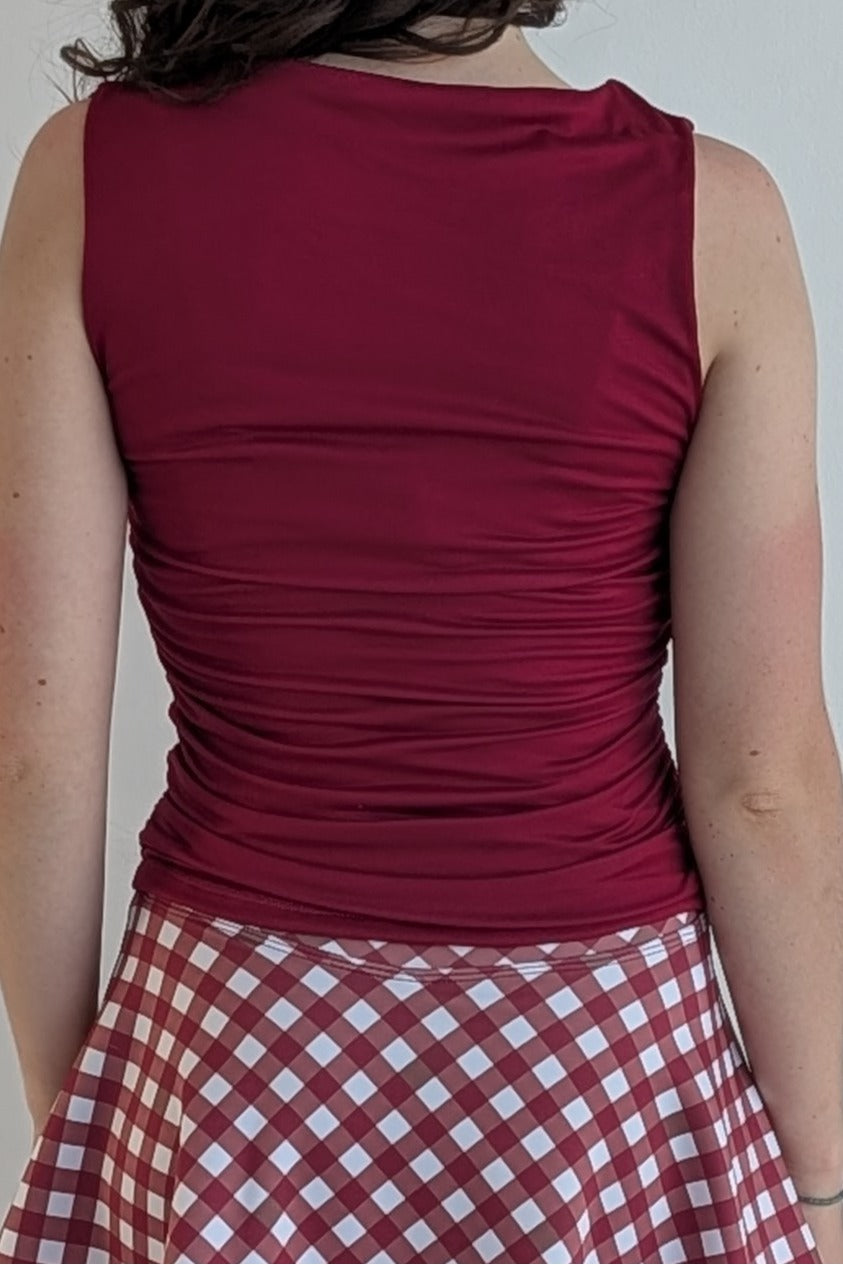 Person wearing a crimson sleeveless top and a red and white checkered skirt against a plain background