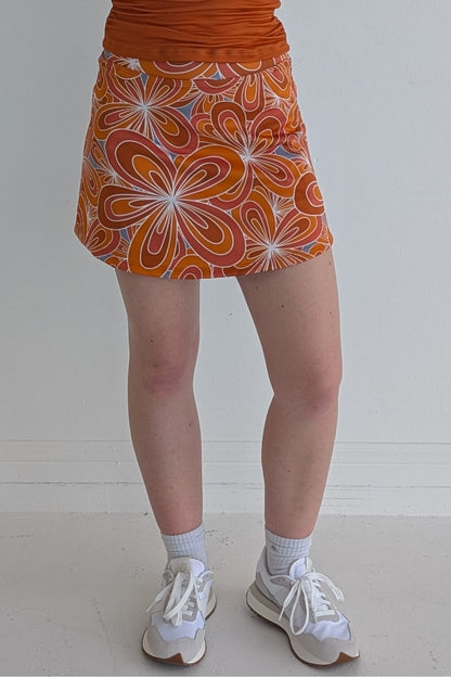 Form Fitting burnt orange miniskirt with 70's inspired flower print and built in shorts and pockets; great for gameday or hanging out with friends.