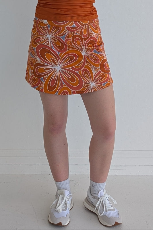 Form Fitting burnt orange miniskirt with 70's inspired flower print and built in shorts and pockets; great for gameday or hanging out with friends.