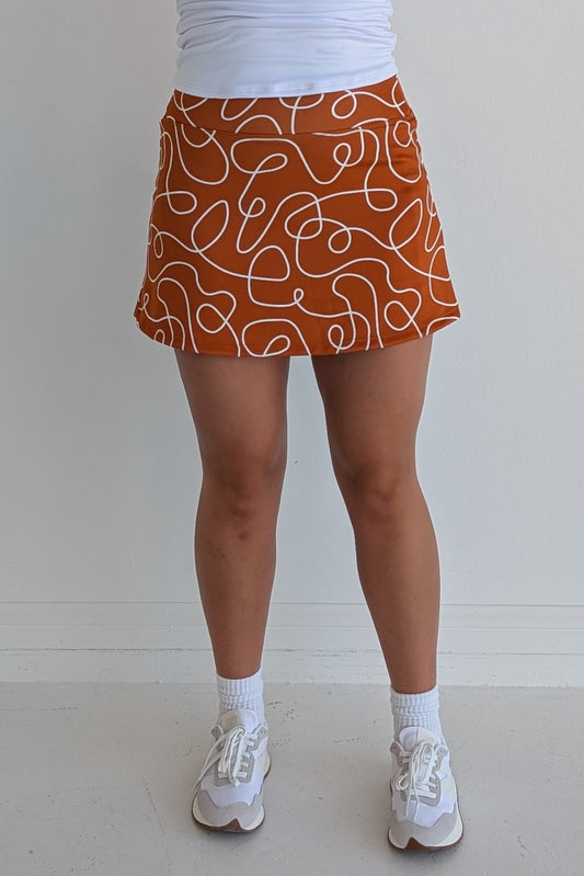 Form Fitting burnt orange miniskirt with scribbles print and built in shorts and pockets; great for gameday or hanging out with friends.