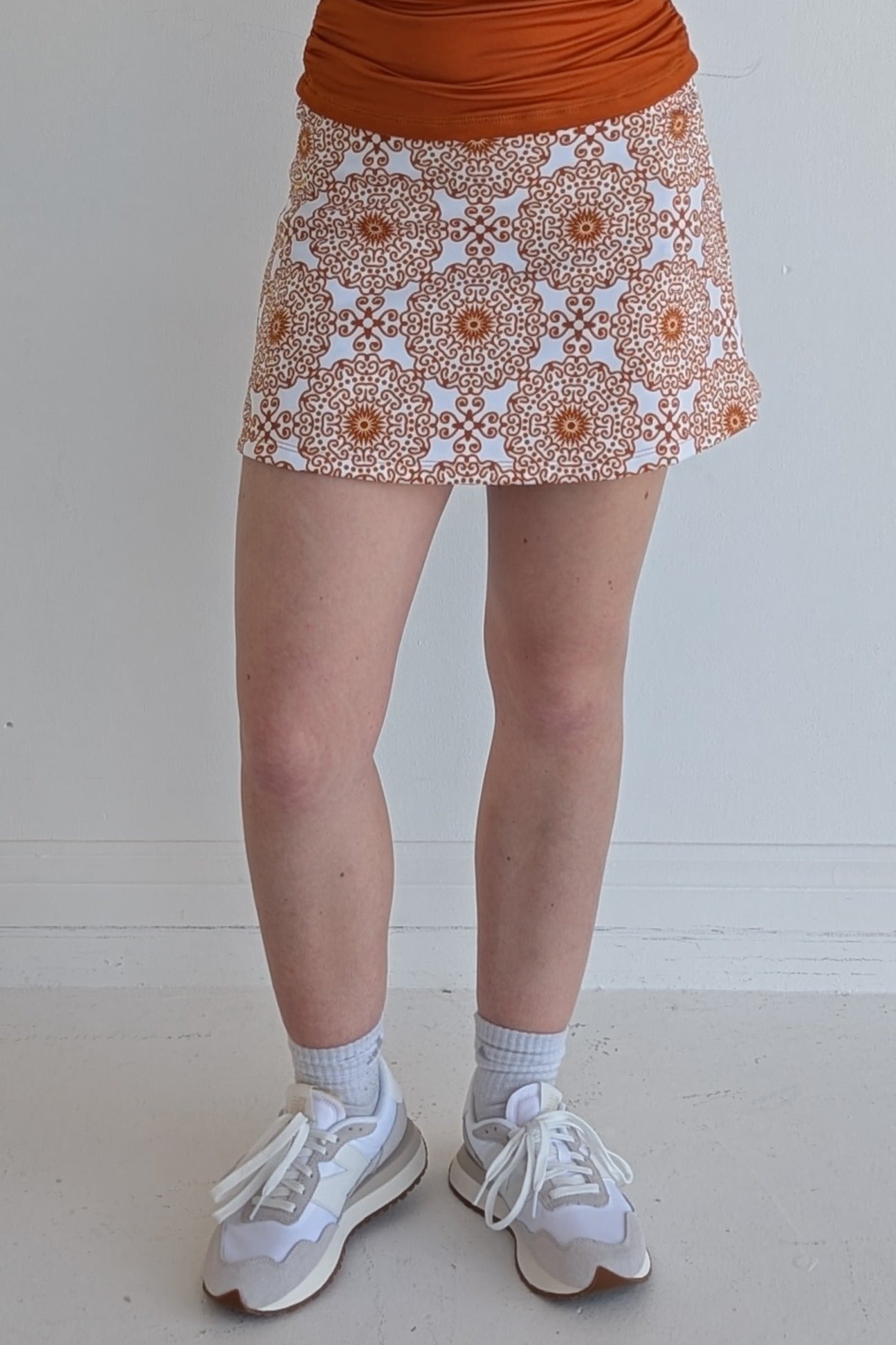 Form Fitting burnt orange miniskirt with scroll print and built in shorts and pockets; great for gameday or hanging out with friends.
