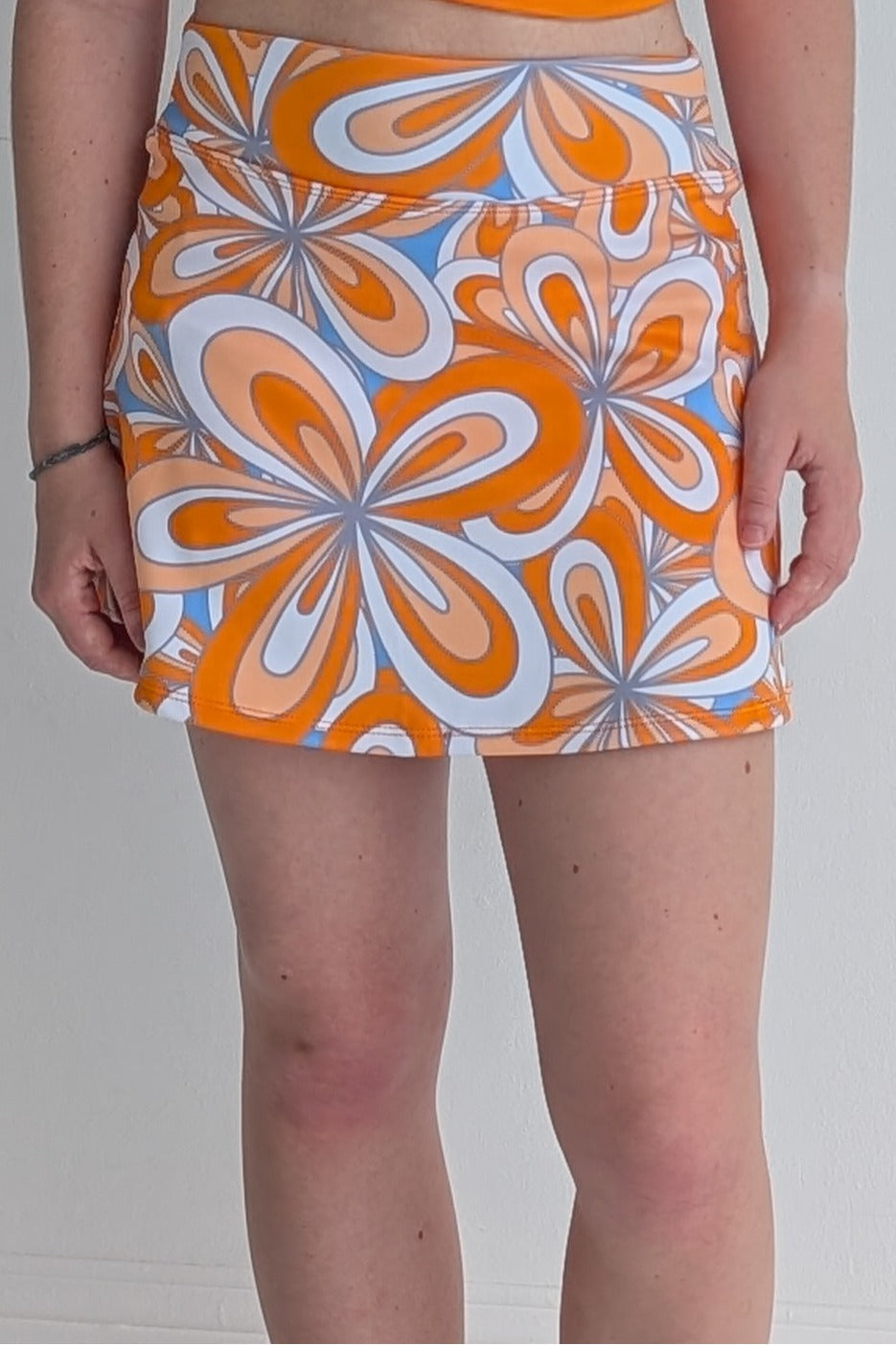 Form Fitting orange miniskirt with 70's inspired flower print and built in shorts and pockets; great for gameday or hanging out with friends.