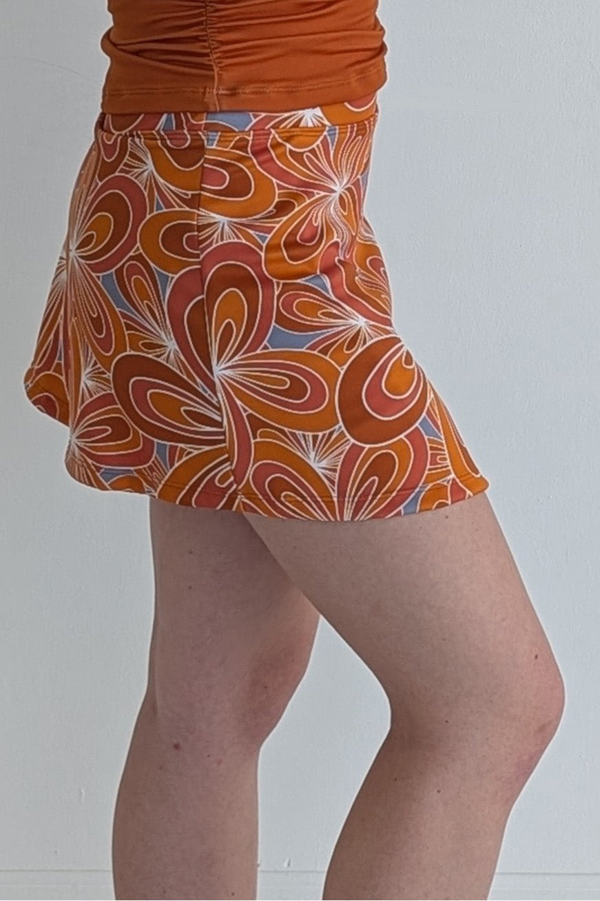 Form Fitting burnt orange miniskirt with 70's inspired flower print and built in shorts and pockets; great for gameday or hanging out with friends.