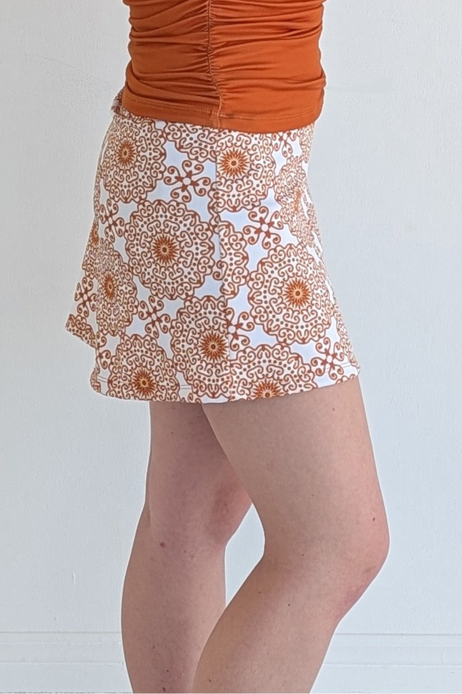 Form Fitting burnt orange miniskirt with scroll print and built in shorts and pockets; great for gameday or hanging out with friends.