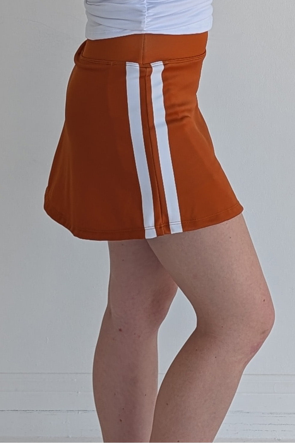 Form Fitting burnt orange miniskirt with side stripes and built in shorts and pockets; great for gameday or hanging out with friends.