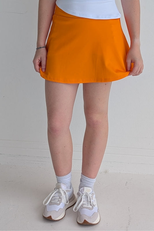 Relaxed back solid orange miniskirt with built in shorts and pockets; great for gameday or hanging out with friends.