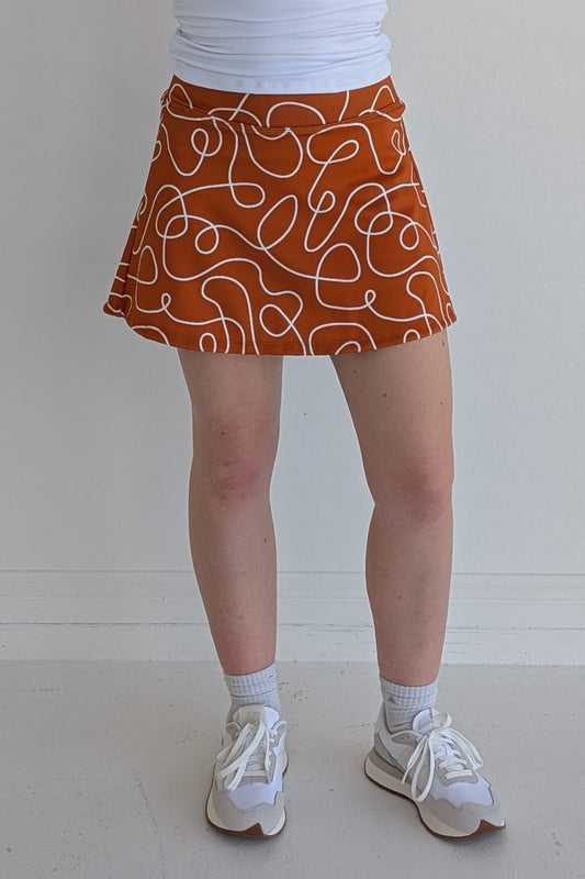 Relaxed back burnt orange miniskirt with scribbles print and built in shorts and pockets; great for gameday or hanging out with friends.