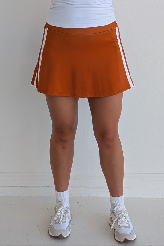 Relaxed back burnt orange miniskirt with side stripes and built in shorts and pockets; great for gameday or hanging out with friends.