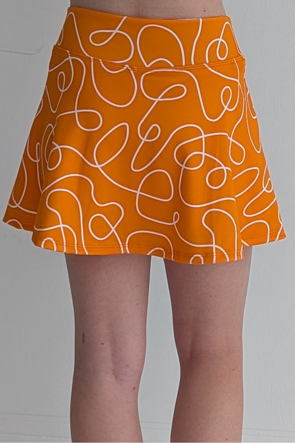 Relaxed back orange miniskirt with scribbles print and built in shorts and pockets; great for gameday or hanging out with friends.