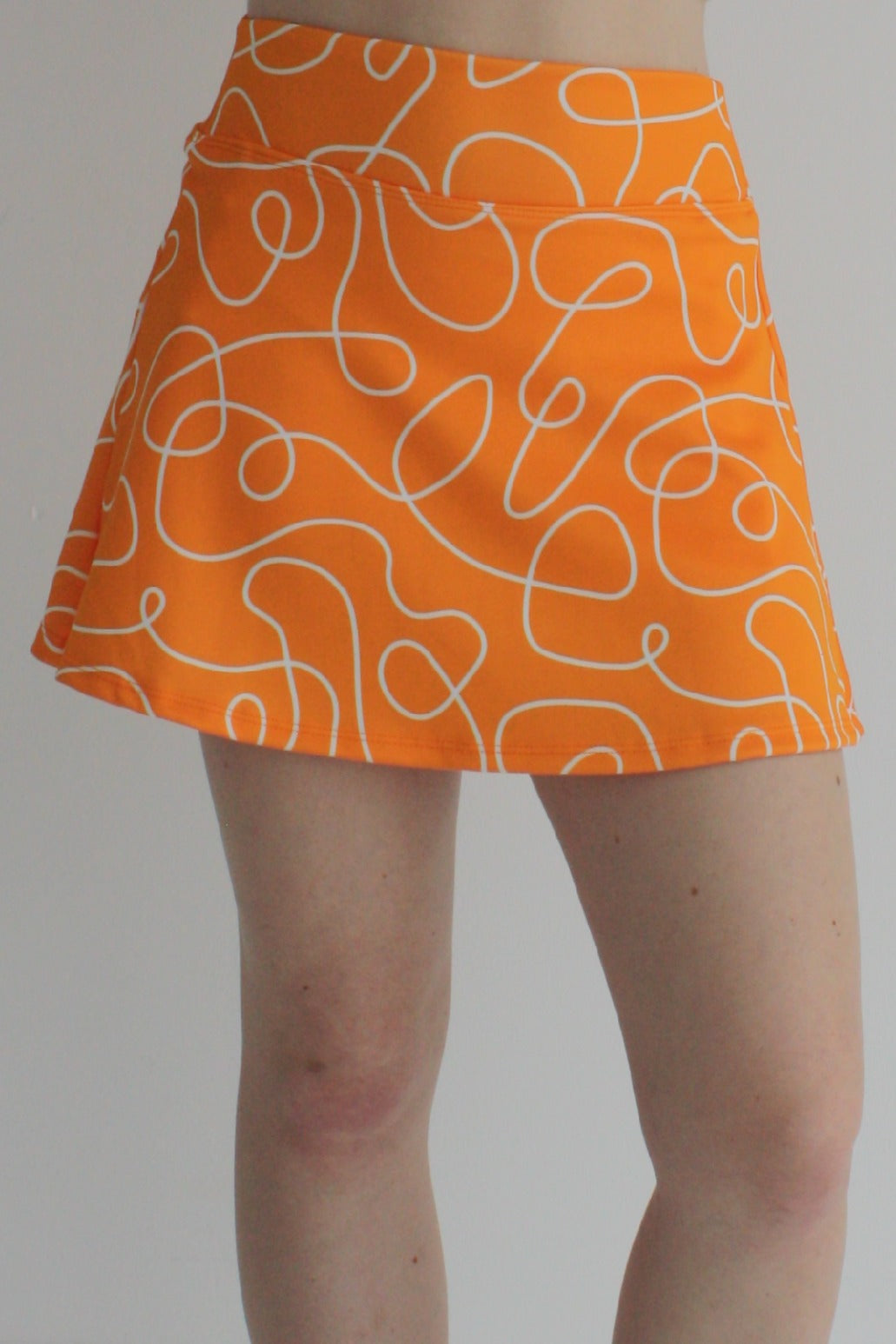 Relaxed back orange miniskirt with scribbles print and built in shorts and pockets; great for gameday or hanging out with friends.