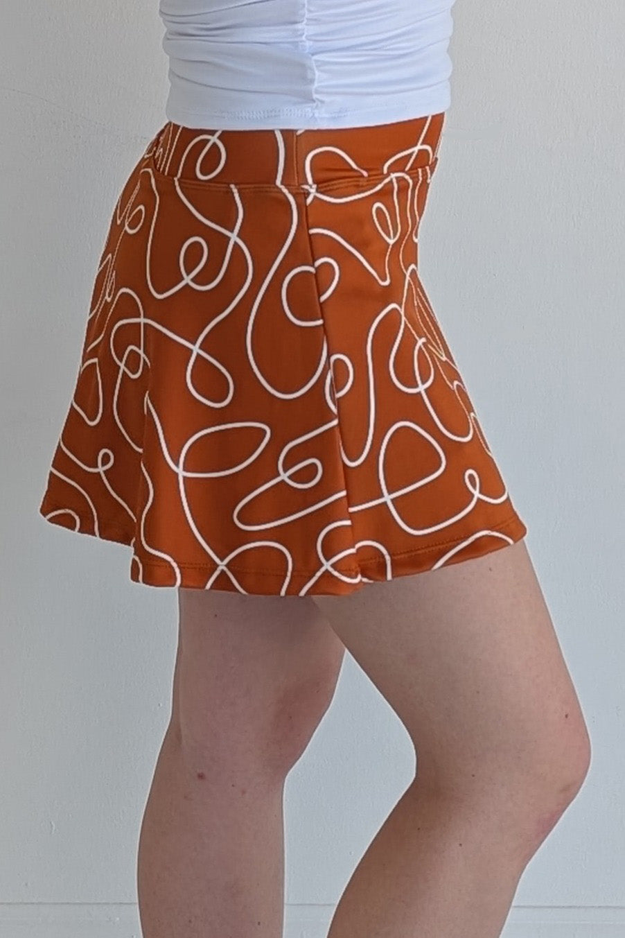 Relaxed back burnt orange miniskirt with scribbles print and built in shorts and pockets; great for gameday or hanging out with friends.