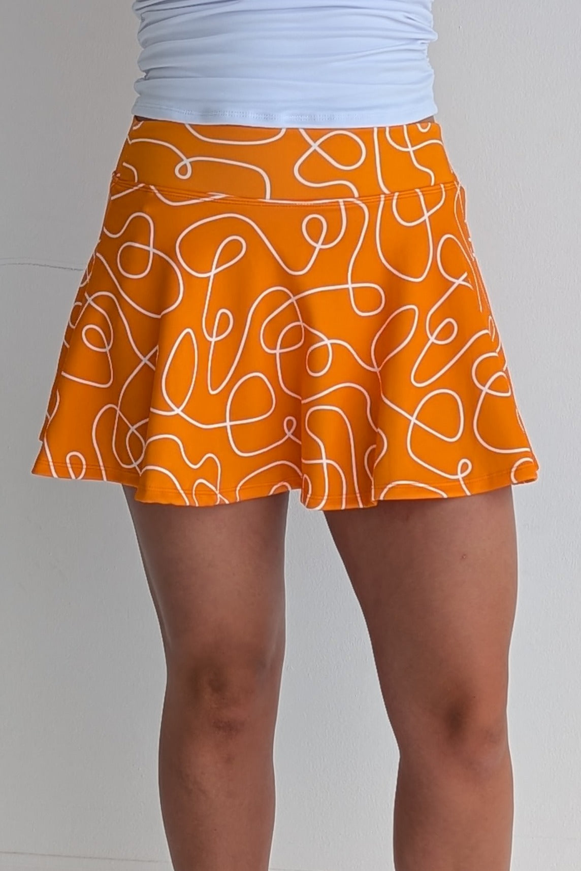 Full bodied orange miniskirt with scribbles print and built in shorts and pockets; great for gameday or hanging out with friends.