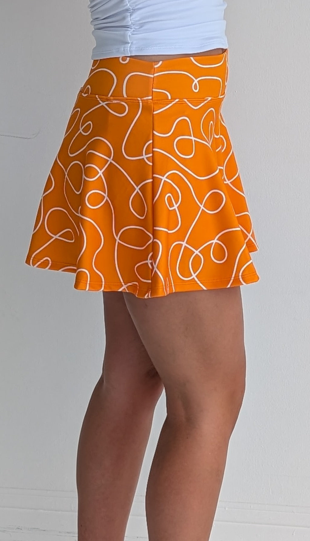 Full bodied orange miniskirt with scribbles print and built in shorts and pockets; great for gameday or hanging out with friends.